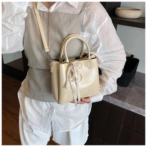 Close-up of cream leather bucket bag with pearl bow charm on shoulder strap
