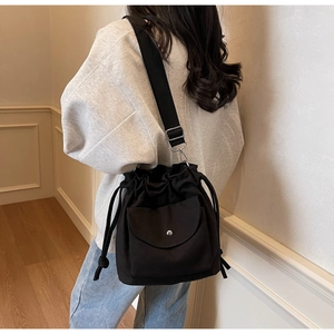 Détail du sac seau en toile noire avec fermeture à cordon et poche avant à rabat