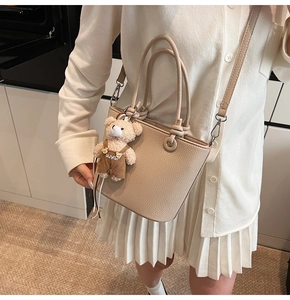 Dettaglio borsa a secchiello beige in pelle con ciondolo a forma di orsetto di peluche