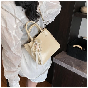 Detail of cream bucket bag with elegant pearl bow charm and detachable shoulder strap