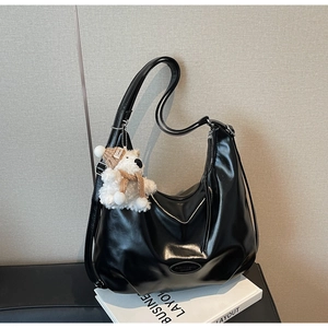 Détail du sac hobo en cuir noir brillant avec un pendentif ours en peluche et un logo