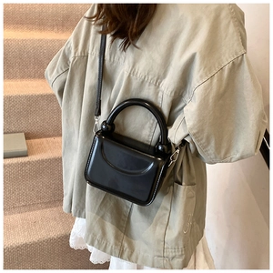 Close-up of black patent leather mini handbag with round handle and detachable strap