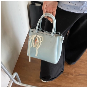 Detail of light blue leather bucket bag with pearl bow and doll charm accessory