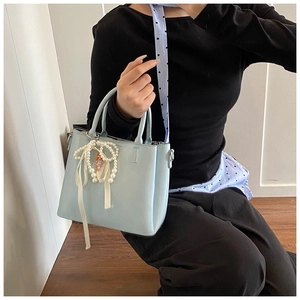 Detail shot of light blue bucket bag featuring a pearl bow charm and twin handles