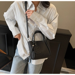 Détail d'un sac à main noir en cuir litchi avec breloque chien et gland à cordon