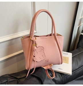 Detail of light pink lychee texture leather bag with embossed bear and gold hardware