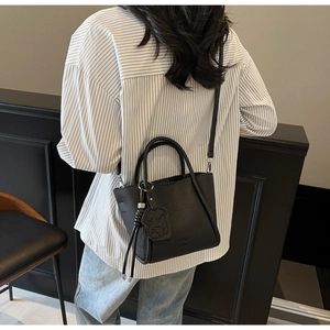Gros plan d'un sac à main noir grainé avec bandoulière et pendentif chien mignon
