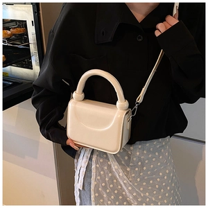 Detail of cream white mini crossbody bag with glossy finish and round handle