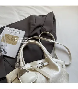 Detail der cremefarbenen Beuteltasche mit Schultergurt und goldenem Herzanhänger