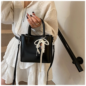 Close-up of black glossy handbag with pearl bow charm and pink doll pendant detail