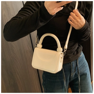 Detail of a creamy white mini square bag featuring a thick round handle and smooth finish