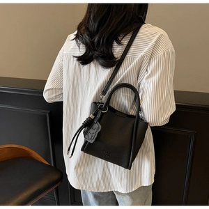 Détail d'un sac à main noir en cuir grainé avec bandoulière et pendentif ours