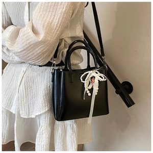 Detail of black bucket bag featuring a white pearl and satin bow charm on textured leather