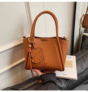 Close-up of brown pebbled leather handbag with PAN TOR logo and cute dog charm detail
