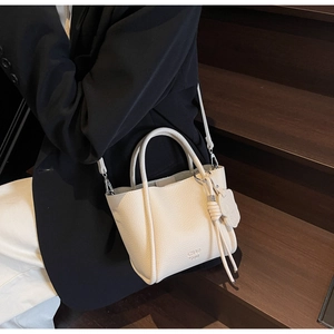 Détail du sac crème en cuir grainé avec logo doré porté sur une marche en bois sombre