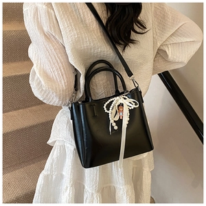 Detail of black bucket bag with pearl strand and silk bow on white dress background