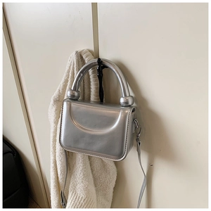 Detail of silver metallic handbag featuring creative ball-joint handle and sleek strap