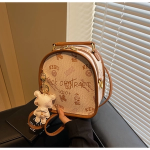 Detail of retro beige round bag with brown trim, graffiti prints, and plush bear charm