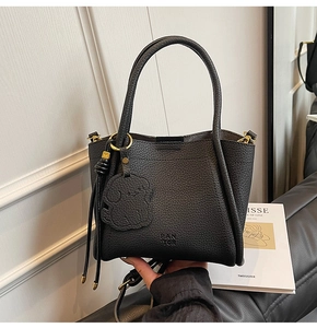 Detail of black lychee grain leather tote bag with gold hardware and puppy charm