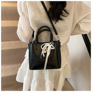 Detail of a black leather bucket bag with white pearls, silk ribbon and adjustable strap
