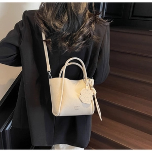 Sac fourre-tout beige grainé avec pendentif d'ours porté par un mannequin en tailleur noir