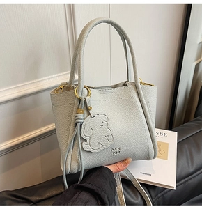 Detail of light grey lychee textured leather tote bag with branded charm and gold hardware