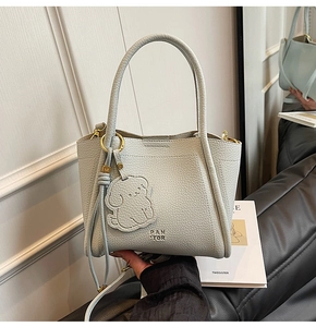 Detail of light gray lychee grain leather bag with PAN TOR logo and bear charm
