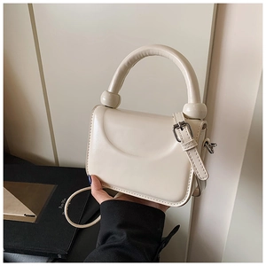 Detail of cream mini handbag with glossy finish, curved handle, and silver buckle strap