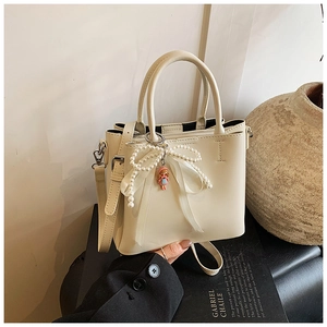 Detail of beige bucket bag featuring pearl bow decoration and cute doll charm accessory