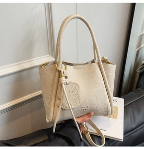 Close-up of cream pebble grain leather handbag with cute bear relief and gold hardware
