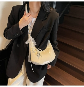 Detail of cream white leather hobo bag featuring pearl bow and silver heart charm