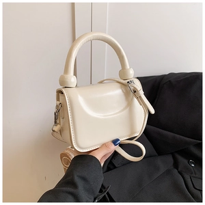 Detailed macro view of the cream-colored glossy PU leather handbag with metal buckle