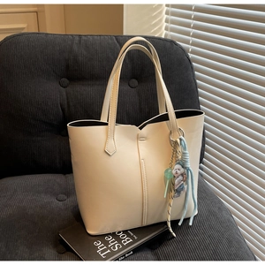 Detail of a minimalist cream tote bag with a cartoon dog charm on a corduroy sofa