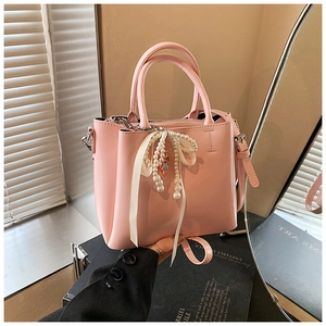 Close-up of light pink bucket bag with cream ribbon bow and elegant pearl charms