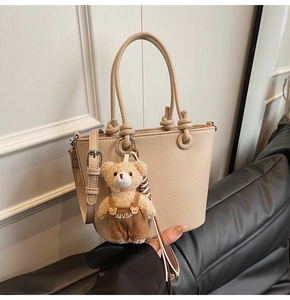 Dettaglio borsa a secchiello in pelle beige a grana con ciondolo a forma di orsetto
