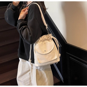 Détail du sac seau en toile beige à cordon avec poche externe sur un escalier vintage