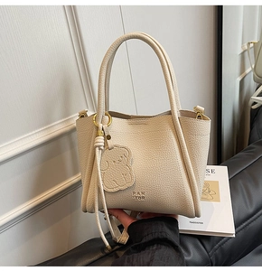 Detail of creamy white pebble grain leather tote bag with PAN TOR logo and bear charm