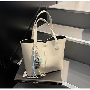 Detail of cream leather tote bag featuring plush bear charm and decorative cords on straps