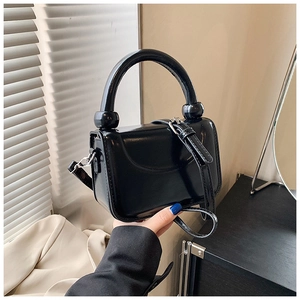 Detail of glossy black handbag with distinctive ball-joint handle and sleek leather texture