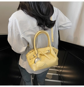 Bolso cubo de cuero amarillo pálido con colgante de corazón mostrado en modelo