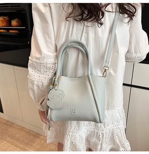 Detail of light blue lychee pattern leather bucket bag with dog charm and brand logo