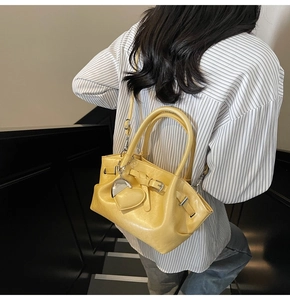 Detalle del bolso tipo cubo amarillo con colgante de corazón llevado por una modelo
