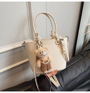 Dettaglio di borsa a secchiello bianca con trama litchi e ciondolo a forma di orsetto