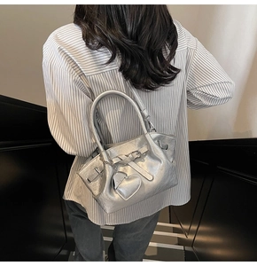 Detalle de bolso tipo cubo en cuero plateado con hebillas decorativas y corazón