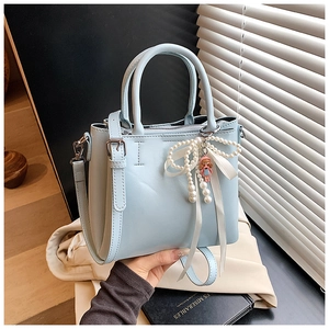 Detail of light blue bucket bag with pearl bow charm and cute girl doll accessory