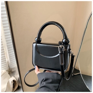 Detail of minimalist black square handbag with smooth finish and curved handle