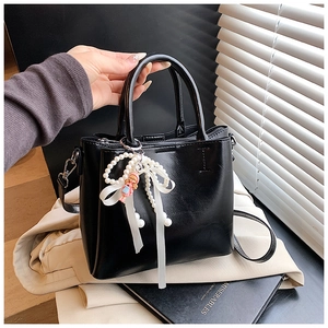 Detail of black bucket bag with pearl pendant, bow, and charm in elegant setting
