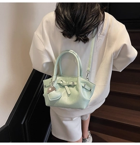 Detalle de bolso tipo cubo verde menta con colgante de corazón mostrado en una modelo