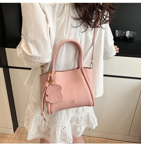 Detailed view of pink crossbody bucket bag with dog charm and gold hardware on model