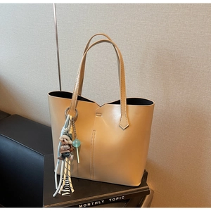 Detail of minimalist cream tote bag with asymmetric stitching and plush puppy pendant decoration